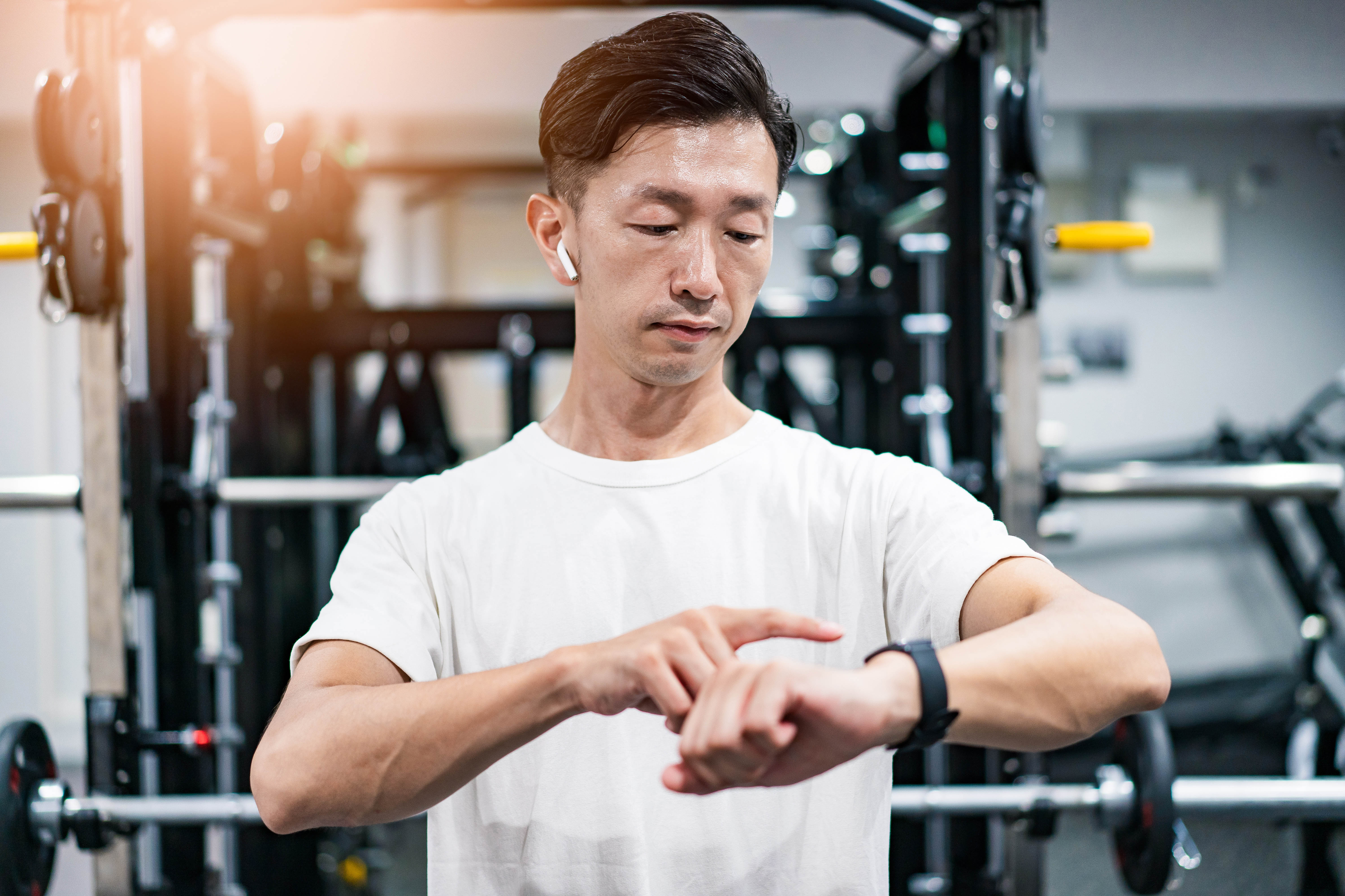 Middle aged Asian man in the gym checking his smart watch. He also has his headphones in.